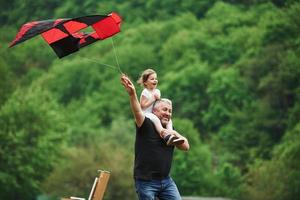 Everyone is happy. Running with red kite. Child sitting on the man's shoulders. Having fun photo