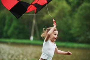 Red and black colored kite. Positive female child running outdoors photo