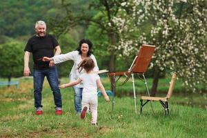 In casual clothes. Grandmother and grandfather have fun outdoors with granddaughter. Painting conception photo