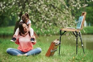 Closeness of the people. Mother and daughter sitting near easel in the park at spring time photo