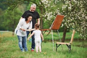 Asking for a try. Grandmother and grandfather have fun outdoors with granddaughter. Painting conception photo