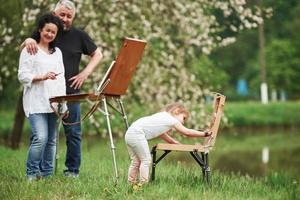 Grandmother and grandfather have fun outdoors with granddaughter. Painting conception photo