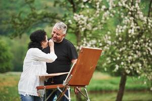 Playful mood. Mature couple have leisure days and working on the paint together in the park photo
