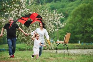 Flowers in hand. Positive female child with grandmother and grandfather running with red and black colored kite in hands outdoors photo