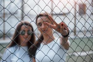 Two female friends stands behind the fence at daytime outdoors photo