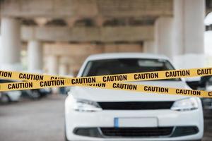 White colored automobile. Yellow caution tape near the car parking lot at daytime. Crime scene photo