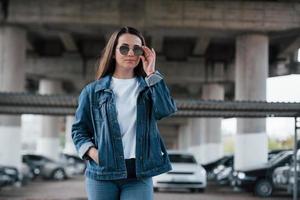 Touching the glasses. Portrait of beautiful young woman standing under the bridge outdoors photo