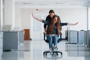 With hands to the sides. Having fun in the office. Young people have a break and driving by using a seat photo