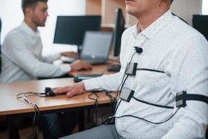 You did not know what your colleague thought. Suspicious man passes lie detector in the office. Asking questions. Polygraph test photo