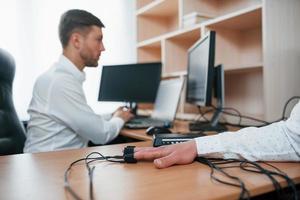 Monitoring heart rate and other different functions of the body. Suspicious man passes lie detector in the office. Asking questions. Polygraph test photo