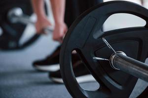 Holding the barbell. Cropped photo of woman doing squatting with barbell in the gym