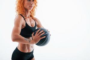 With black soccer ball. Redhead female bodybuilder is in the studio on white background photo