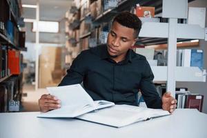 Many of materials. African american man sitting in the library and searching for some information in the books photo