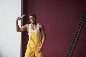 mostrando abdominales. joven trabajador afroamericano en el uniforme amarillo tiene algún trabajo foto