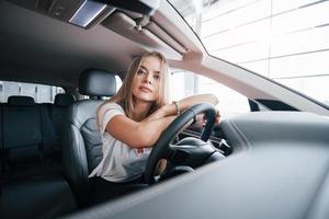 pensando en el futuro. chica en coche moderno en el salón. durante el día en el interior. compra de vehiculo nuevo foto