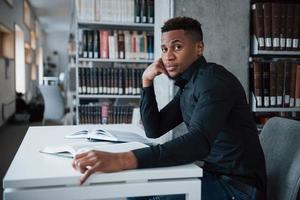 desde el lado. hombre afroamericano sentado en la biblioteca y buscando información en los libros foto