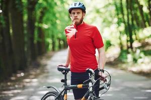 Gorgeous sunlight. Cyclist on a bike is on the asphalt road in the forest at sunny day photo