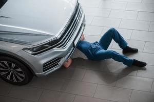 Need to fix one thing quick. Man in blue uniform works with broken car. Making repairings photo