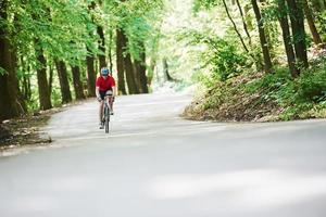 Long way. Cyclist on a bike is on the asphalt road in the forest at sunny day photo