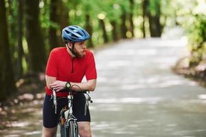 Waiting for a friend. Cyclist on a bike is on the asphalt road in the forest at sunny day photo