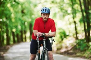 Relaxation between marathon. Cyclist on a bike is on the asphalt road in the forest at sunny day photo