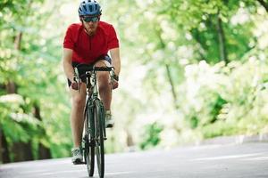 Front view. Cyclist on a bike is on the asphalt road in the forest at sunny day photo