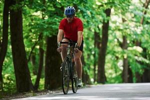 Running forward. Cyclist on a bike is on the asphalt road in the forest at sunny day photo