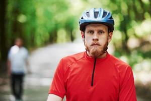 Man in blurred background. Cyclist on a bike is on the asphalt road in the forest at sunny day photo