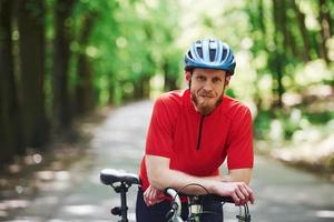 Smiling and relaxing. Cyclist on a bike is on the asphalt road in the forest at sunny day photo