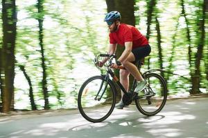 paseo matutino. ciclista en bicicleta está en la carretera asfaltada en el bosque en un día soleado foto