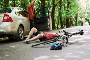 Qué he hecho. víctima en el asfalto. bicicleta y accidente automovilístico de color plateado en la carretera en el bosque durante el día foto