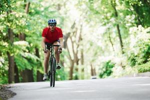 Looking forward. Cyclist on a bike is on the asphalt road in the forest at sunny day photo