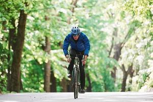 Stamina and strength. Cyclist on a bike is on the asphalt road in the forest at sunny day photo