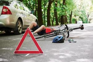 Without consciousness. Victim on the asphalt. Bicycle and silver colored car accident on the road at forest at daytime photo