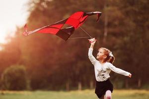 Summertime happiness. Cute girl in casual clothes running with kite in the field. Beautiful nature photo