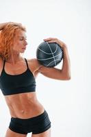 Posing for a camera with soccer ball. Particle view. Redhead female bodybuilder is in the studio on white background photo