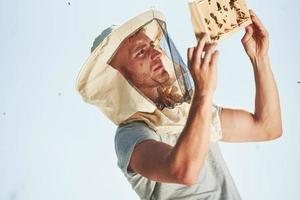 Clear sky. Beekeeper works with honeycomb full of bees outdoors at sunny day photo