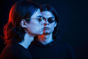 Looking in front and to the side. Portrait of twin brothers. Studio shot in dark studio with neon light photo