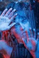 Cool temperature. Studio shot in dark studio with neon light. Portrait of beautiful girl behind wet glass photo