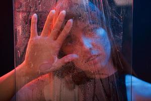 uñas blancas. foto de estudio en estudio oscuro con luz de neón. retrato de una chica hermosa detrás de un vidrio mojado