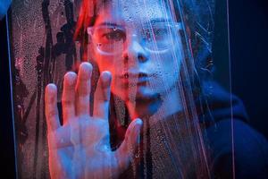 Creative and futuristic concept. Studio shot in dark studio with neon light. Portrait of serious man behind the wet glass photo