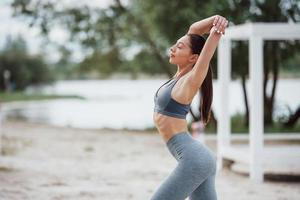 Good morning time. Brunette with nice body shape in sportive clothes have fitness day on a beach photo