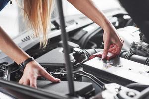 Remowing old battery. Car addicted woman repairs black car indoors in garage at daytime photo