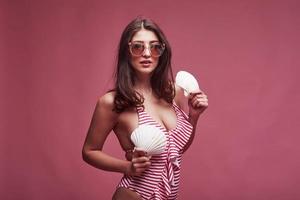 Souvenirs in hands. Stylish beautiful young girl in bikini stands and posing in the studio photo