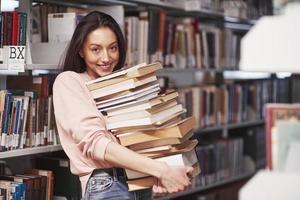 Holds many of books. Brunette girl in casual clothes having good time in the library photo