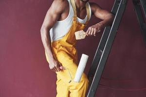 Tools in hands. Young african american worker in the yellow uniform have some job photo