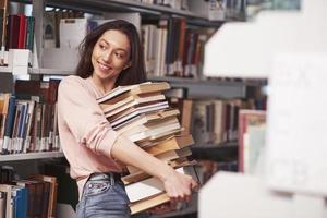 More than enough. Brunette girl in casual clothes having good time in the library full of books photo