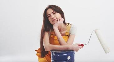 Industrial work. Brunette woman in yellow uniform sits against white background in the studio photo