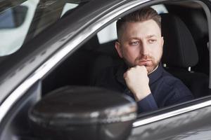 esperando empleado. hombre con ropa oficial probando su auto nuevo en el salón del automóvil foto