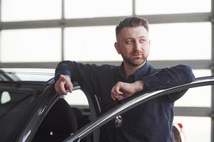 Confident and satisfied. Man in official clothes trying his new car in automobile salon photo